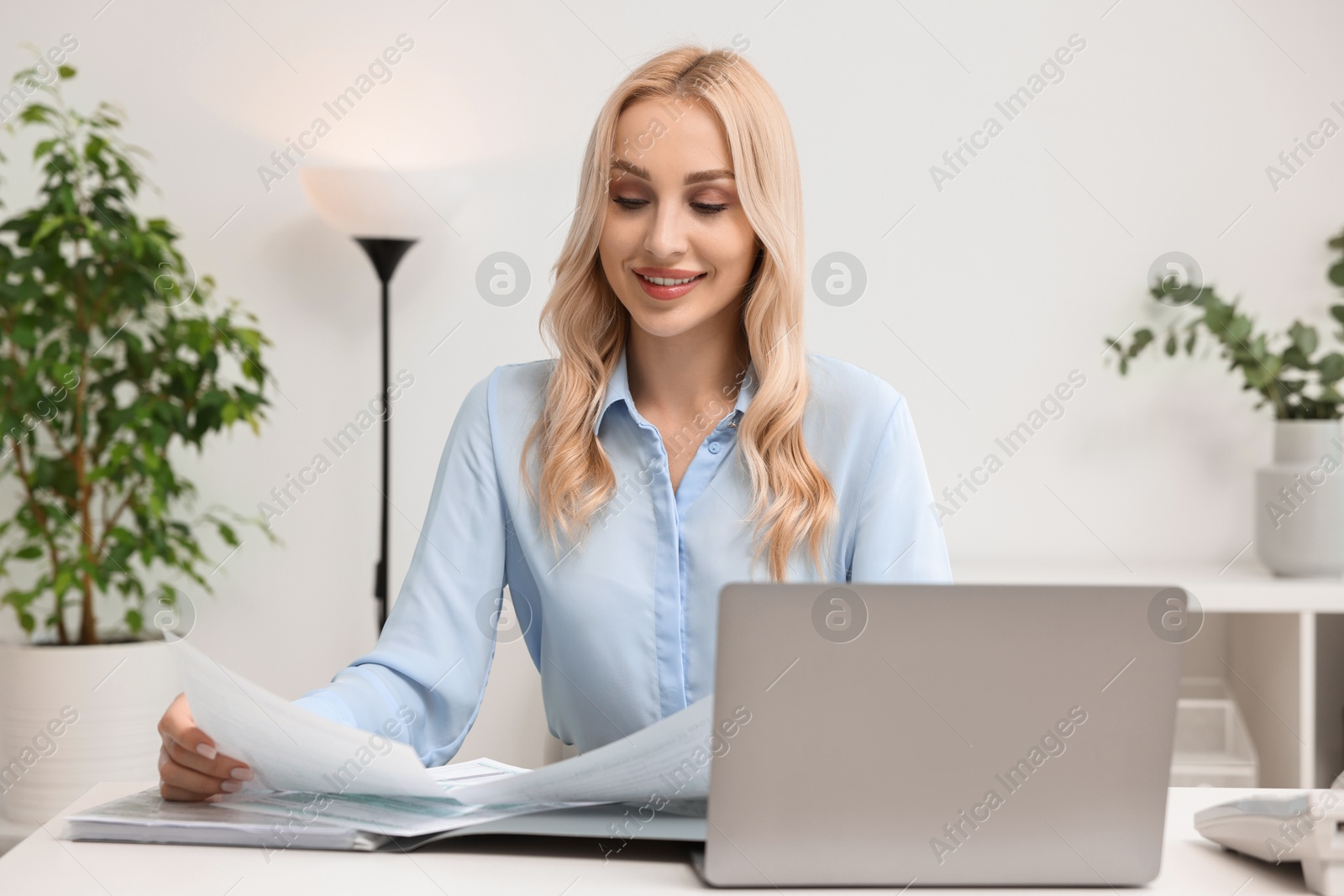 Photo of Happy secretary working with documents at table in office