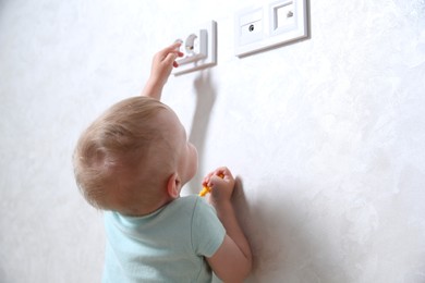 Photo of Little child playing with electrical socket indoors. Dangerous situation