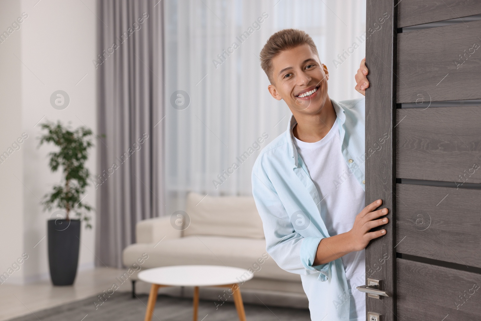 Photo of Happy man standing near door, space for text. Invitation to come indoors