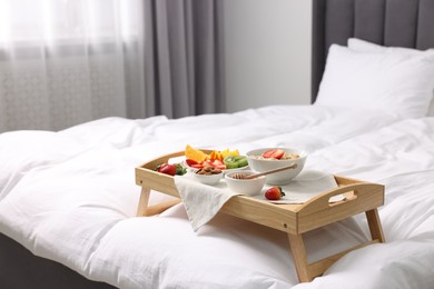 Photo of Wooden tray with tasty breakfast on bed at home