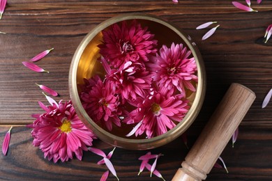 Photo of Tibetan singing bowl with water, beautiful flowers and mallet on wooden table, top view
