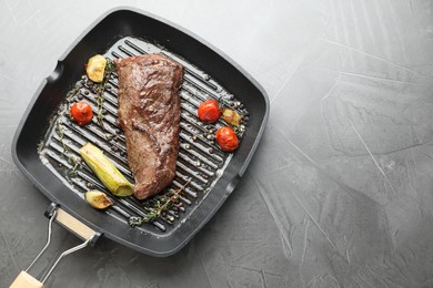 Photo of Delicious grilled beef meat and vegetables in pan on grey table, top view. Space for text