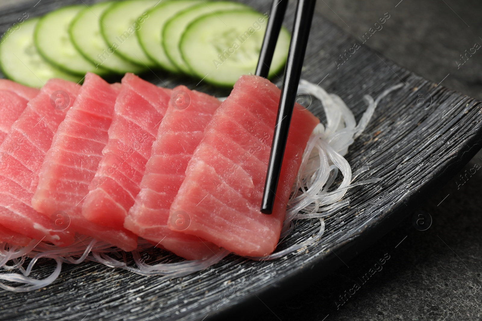 Photo of Taking tasty sashimi (piece of fresh raw tuna) with glass noodles from plate at table, closeup