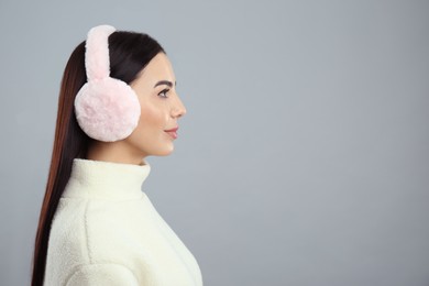 Photo of Beautiful young woman wearing earmuffs on light grey background. Space for text
