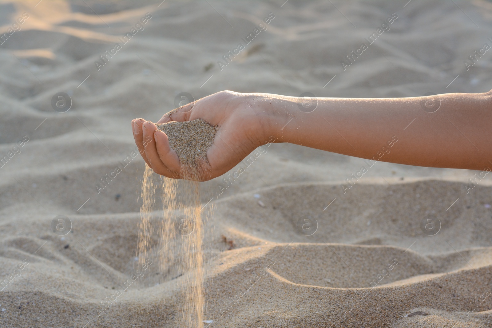 Photo of Girl pouring sand from hand outdoors, closeup. Fleeting time concept