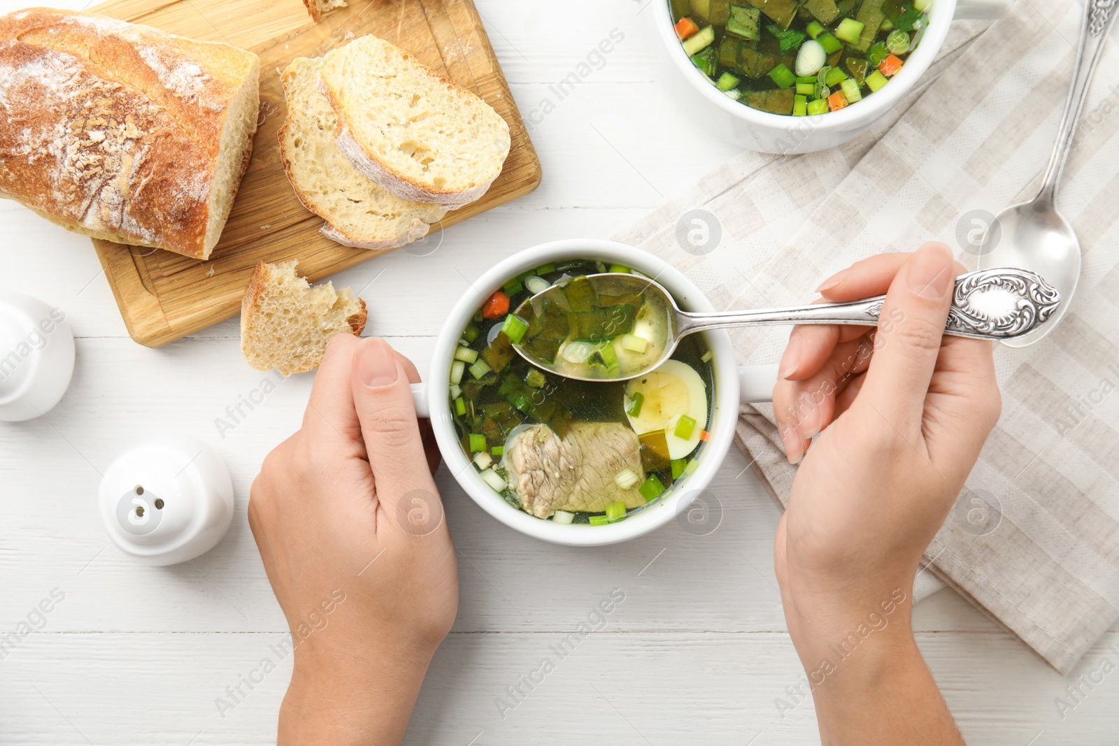 Photo of Woman eating delicious sorrel soup with meat and egg at white wooden table, top view