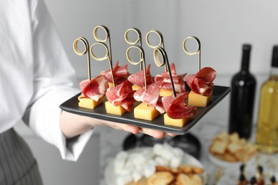 Woman holding plate of tasty canapes with ham and cheese indoors, closeup