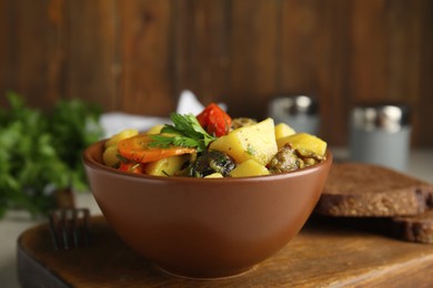 Tasty cooked dish with potatoes in earthenware on wooden board