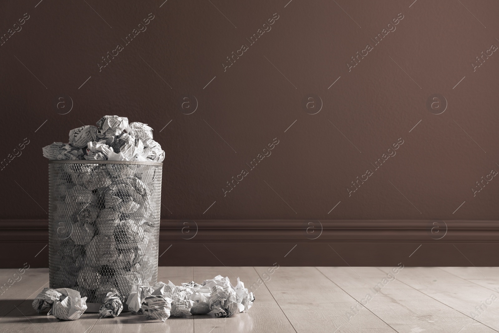 Photo of Metal bin with crumpled paper near brown wall indoors, space for text. Rubbish recycling