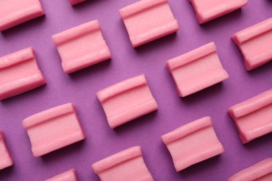 Photo of Tasty pink chewing gums on purple background, flat lay