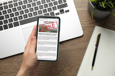 Image of Fake information. Woman using mobile phone to read news at wooden table, closeup. Top view