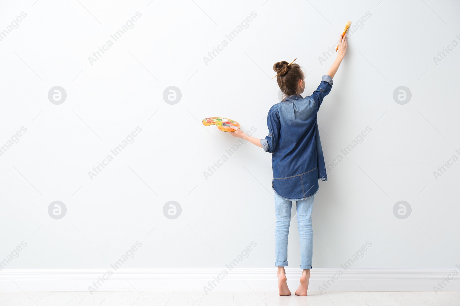 Photo of Little girl painting on light wall indoors, back view. Space for text