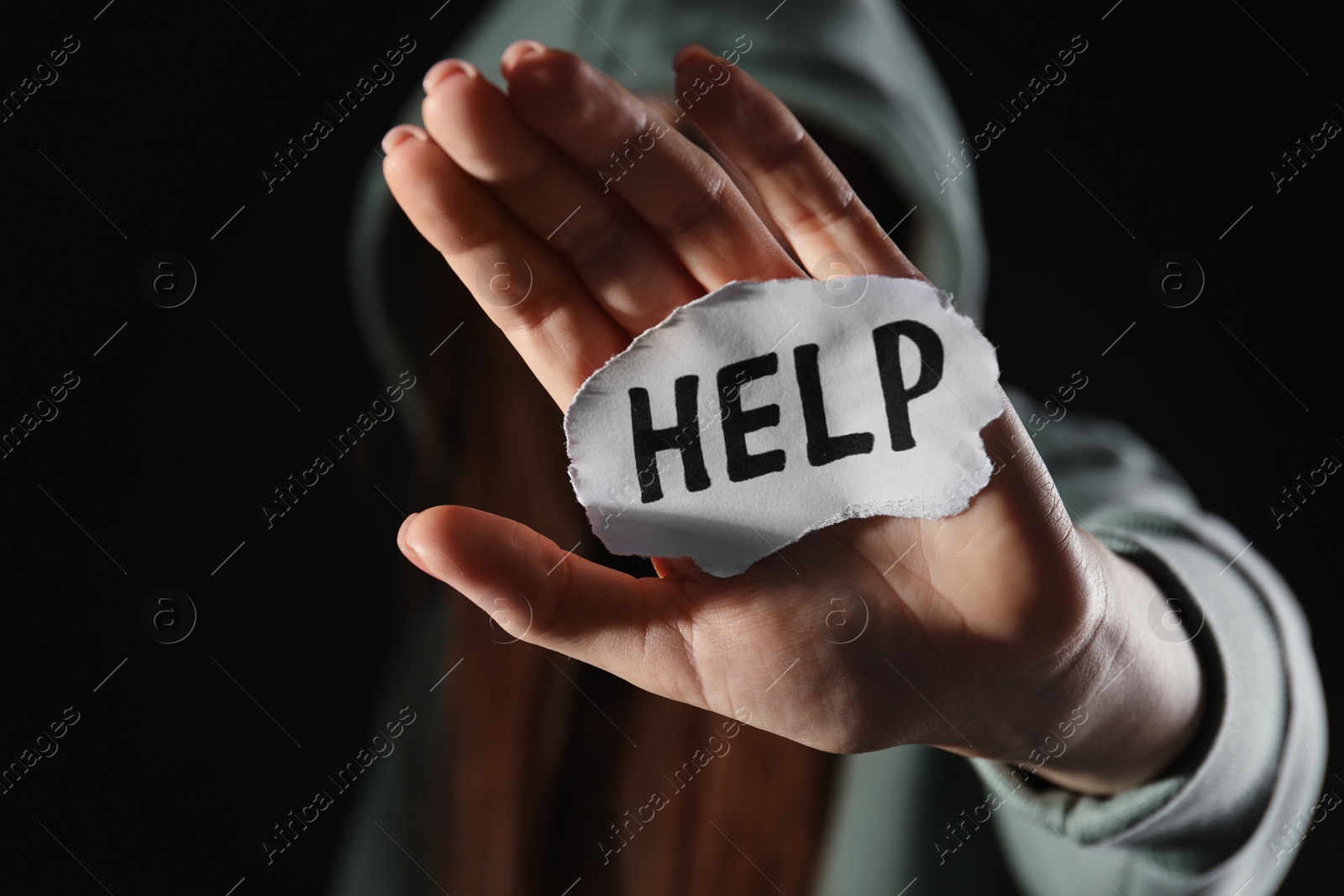 Photo of Woman holding piece of paper with word Help on black background, closeup. Domestic violence concept