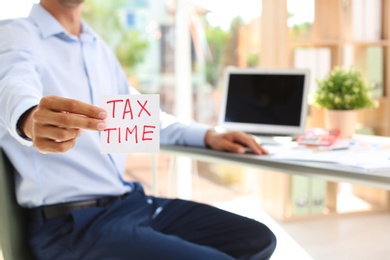 Photo of Man holding card with words TAX TIME indoors