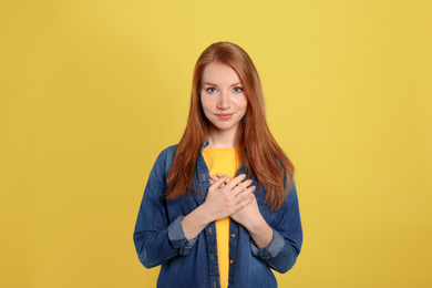 Beautiful grateful woman with hands on chest against yellow background