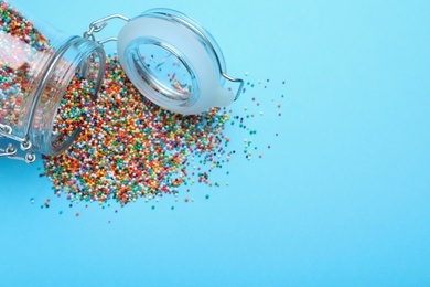 Photo of Colorful sprinkles and jar on light blue background, flat lay with space for text. Confectionery decor