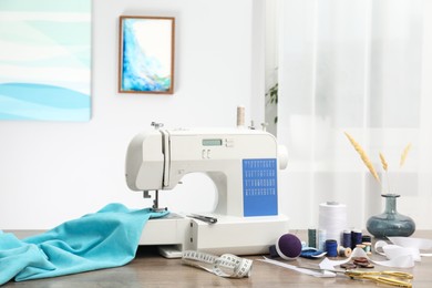 Photo of White sewing machine, cloth and craft accessories on wooden table indoors