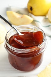 Taking tasty homemade quince jam from jar at white wooden table, closeup