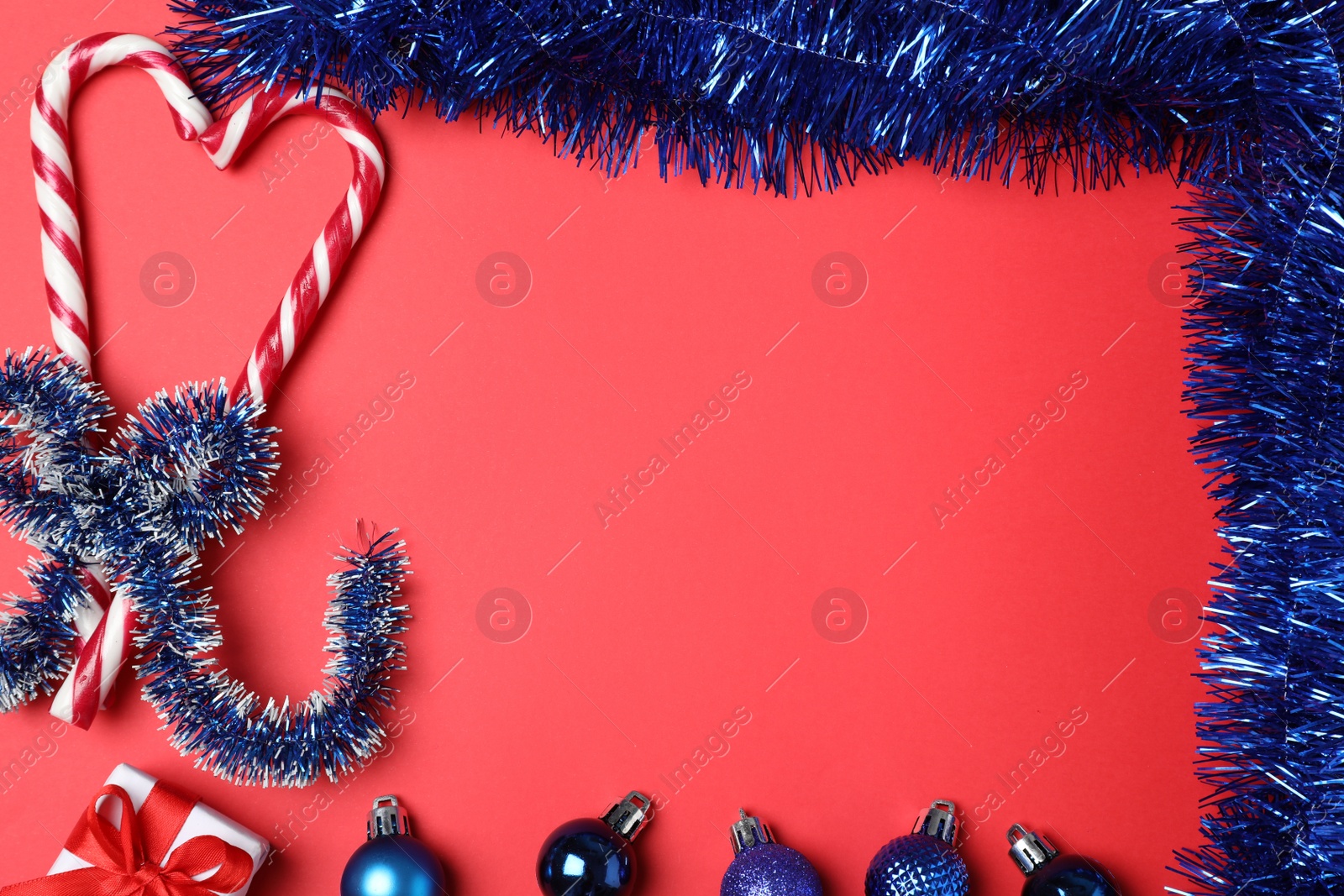 Photo of Frame of bright blue tinsel and Christmas decor on red background, flat lay. Space for text