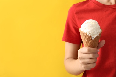 Photo of Woman holding white ice cream in wafer cone on yellow background, closeup. Space for text