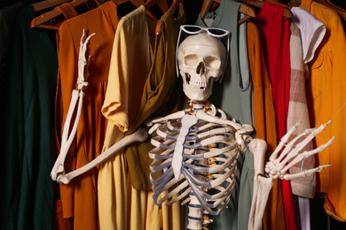 Photo of Artificial human skeleton model among clothes in wardrobe