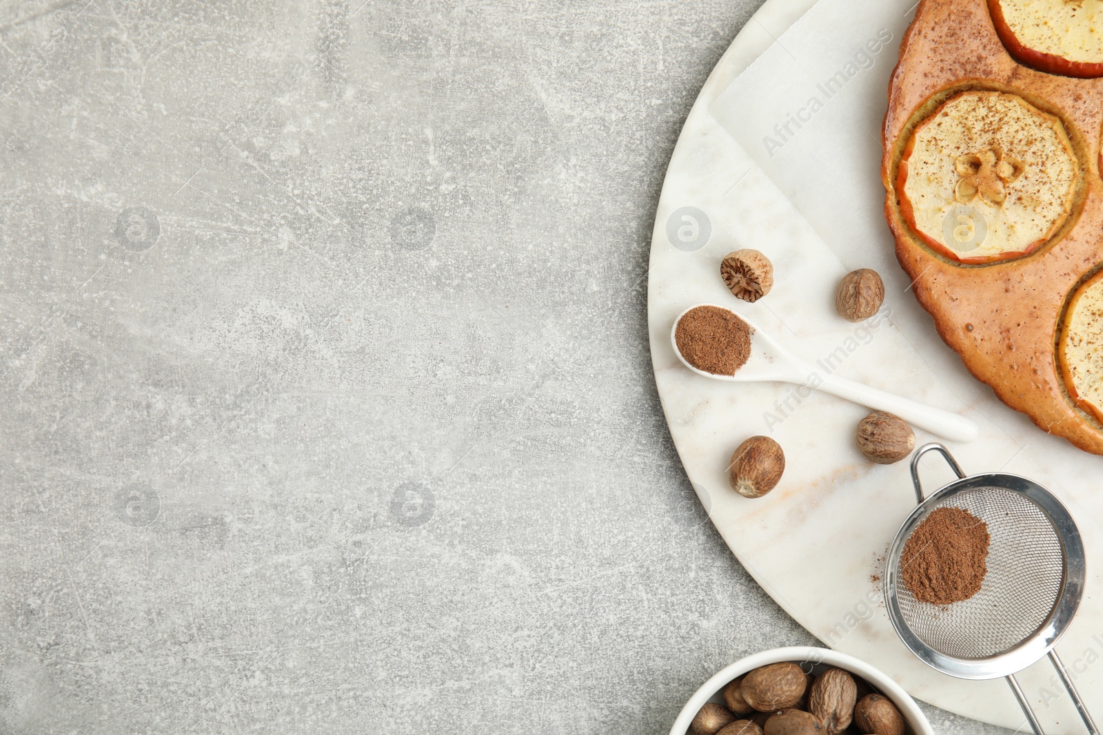 Photo of Nutmeg powder, seeds and tasty apple pie on light grey table, flat lay. Space for text