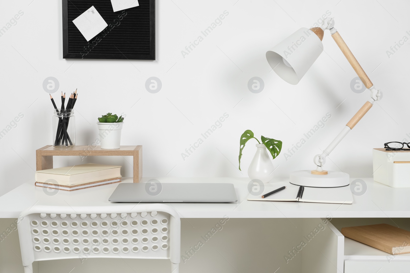 Photo of Cozy workspace with laptop, lamp and stationery on wooden desk at home