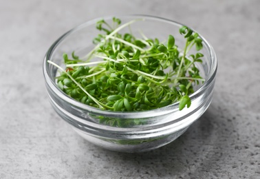 Photo of Fresh organic microgreen in bowl on grey table, closeup