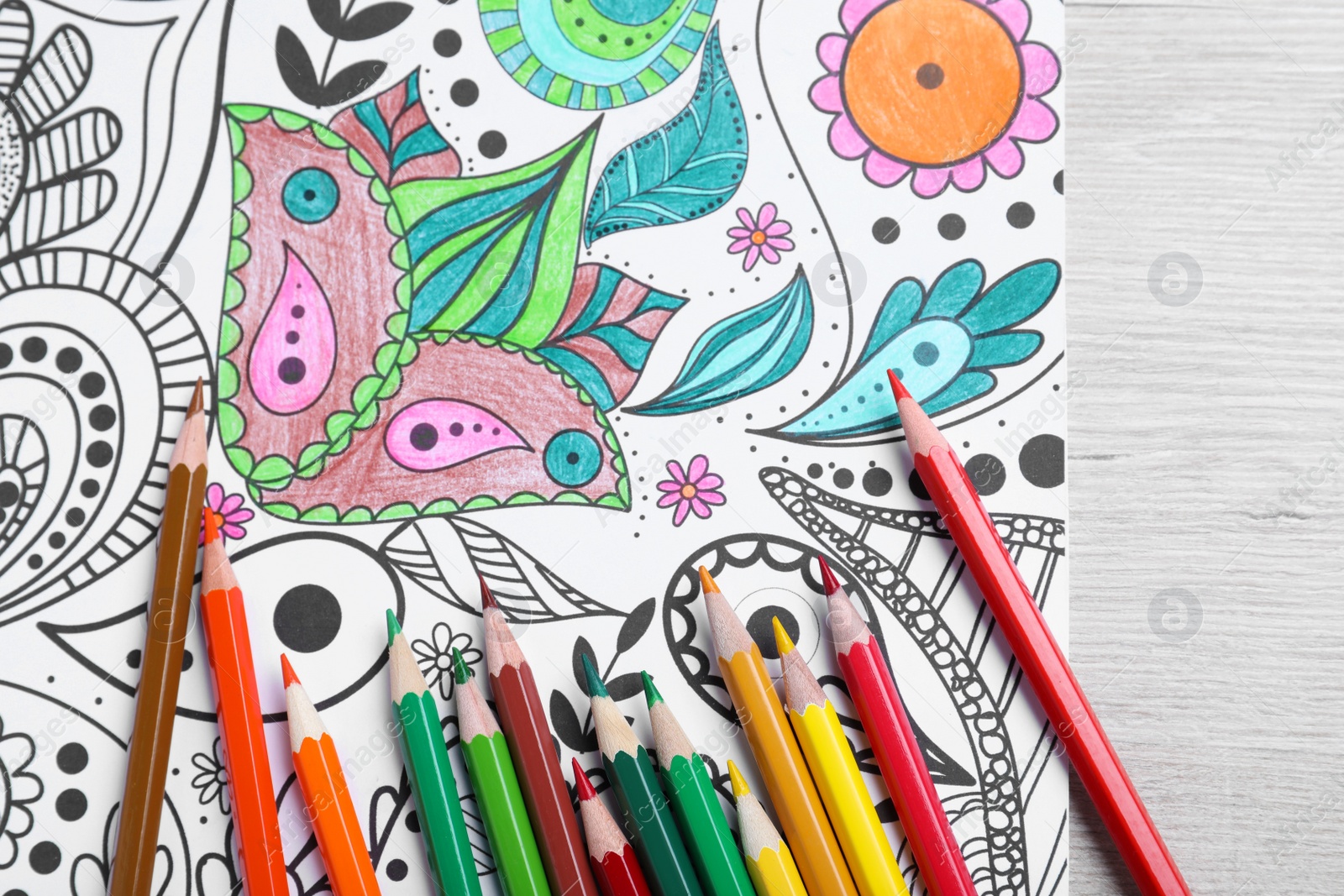 Photo of Antistress coloring page and pencils on light wooden table, flat lay
