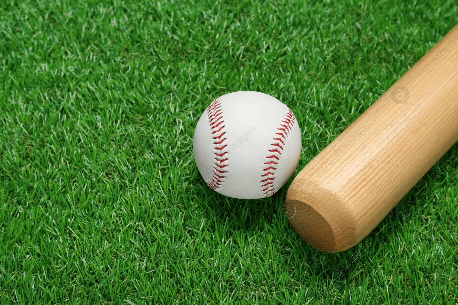 Photo of Wooden baseball bat and ball on green grass, closeup. Sports equipment