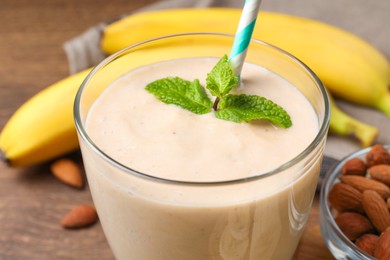 Photo of Glass with banana smoothie and mint on wooden table, closeup