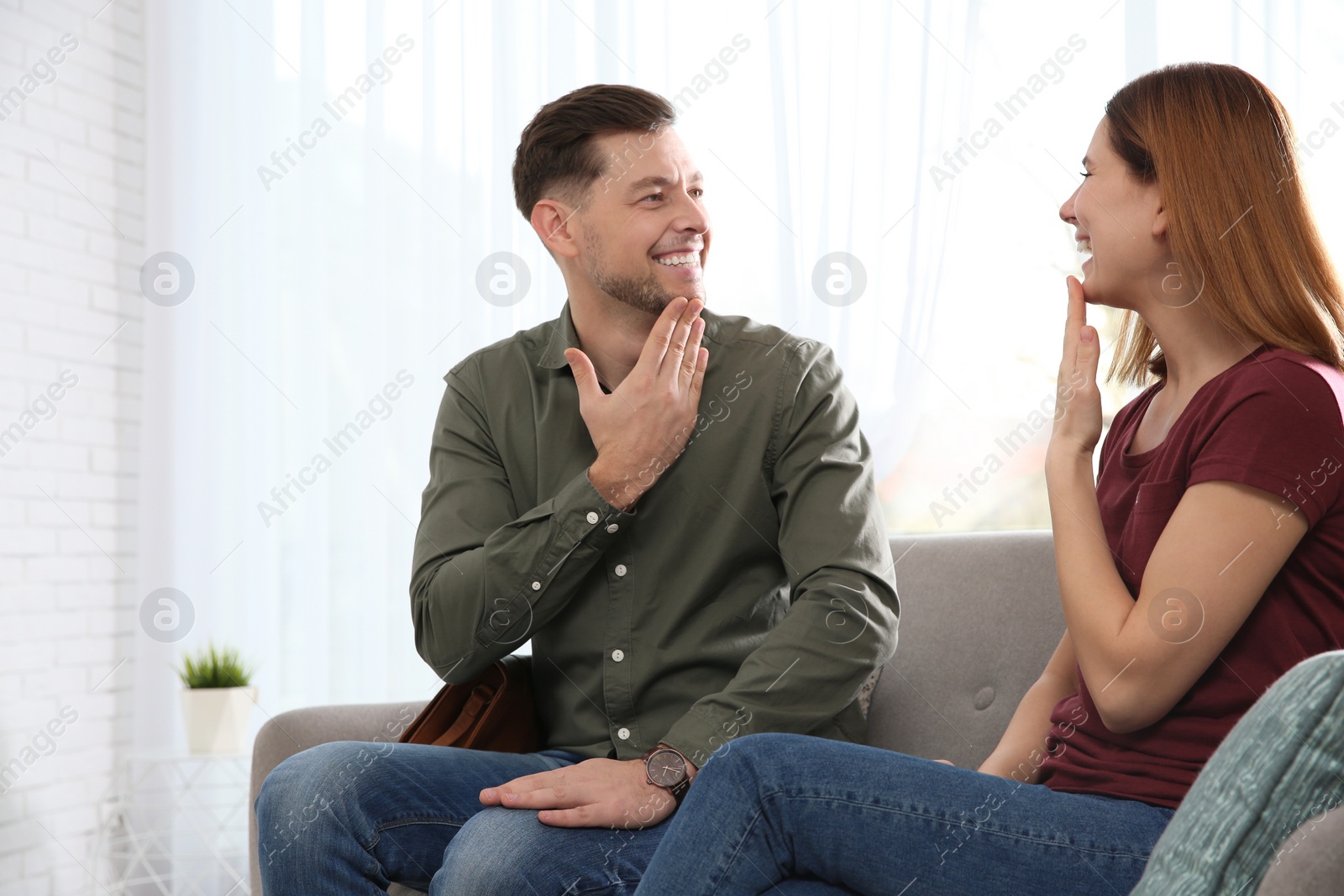 Photo of Hearing impaired friends using sign language for communication on sofa in living room