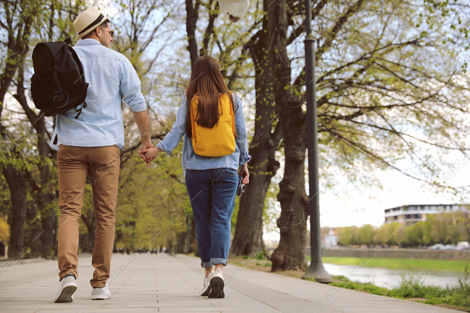 Photo of Couple of tourists with backpacks on city street, back view