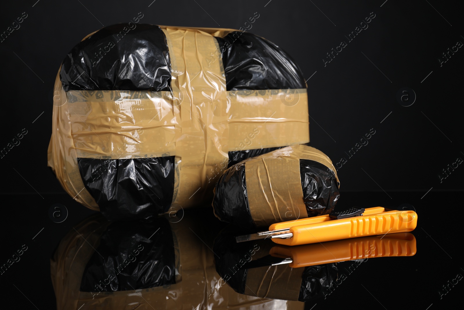 Photo of Smuggling, drug trafficking. Packages with narcotics and utility knife on black mirror surface