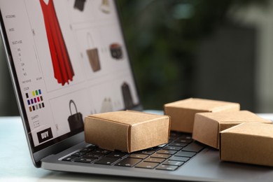 Photo of Online store. Small parcels and laptop on table, closeup. Space for text