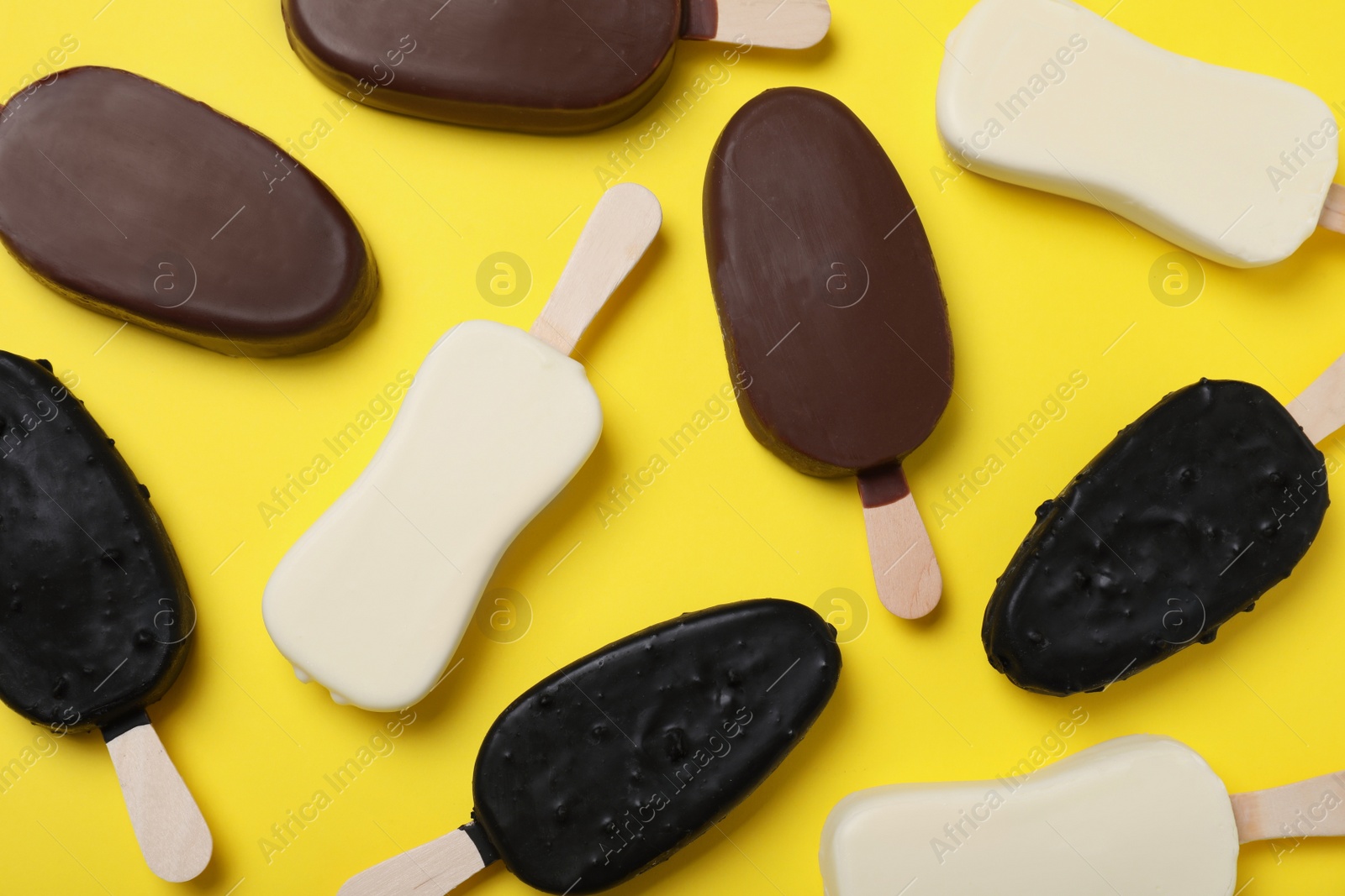 Photo of Different glazed ice cream bars on yellow background, flat lay