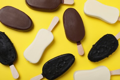 Different glazed ice cream bars on yellow background, flat lay