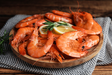 Photo of Delicious cooked shrimps with rosemary and lemon on wooden plate