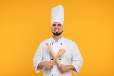 Photo of Happy professional confectioner in uniform holding rolling pin and spatula on yellow background