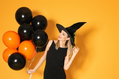 Photo of Beautiful woman wearing witch costume with balloons for Halloween party on yellow background