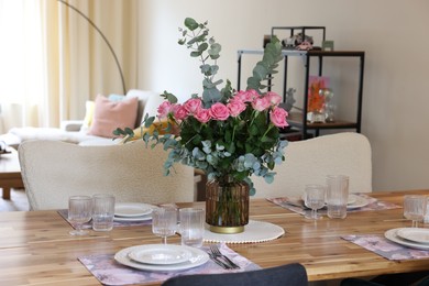 Beautiful table setting with bouquet in dining room. Roses and eucalyptus branches in vase