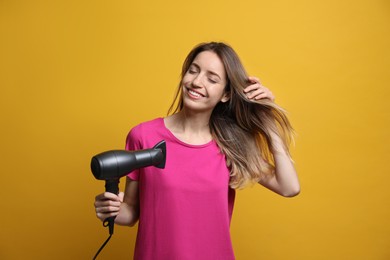 Beautiful young woman using hair dryer on yellow background