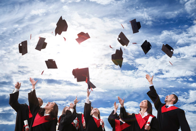 Image of Happy students with diplomas throwing graduation hats in air outdoors