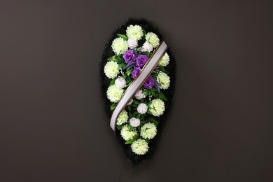 Funeral wreath of plastic flowers with ribbon hanging on dark grey wall