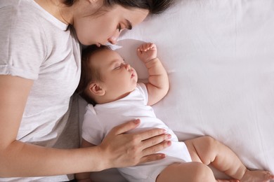 Photo of Young mother resting near her sleeping baby on bed, top view. Space for text