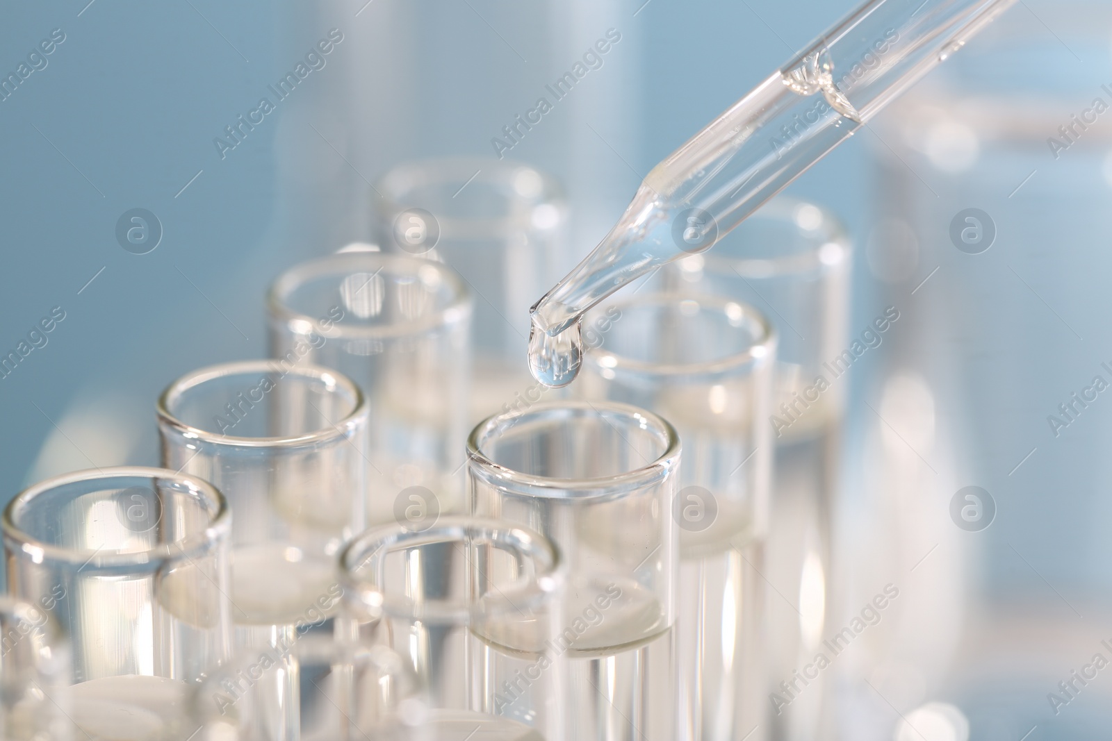 Photo of Laboratory analysis. Dripping liquid from pipette into glass test tube on blurred background, closeup