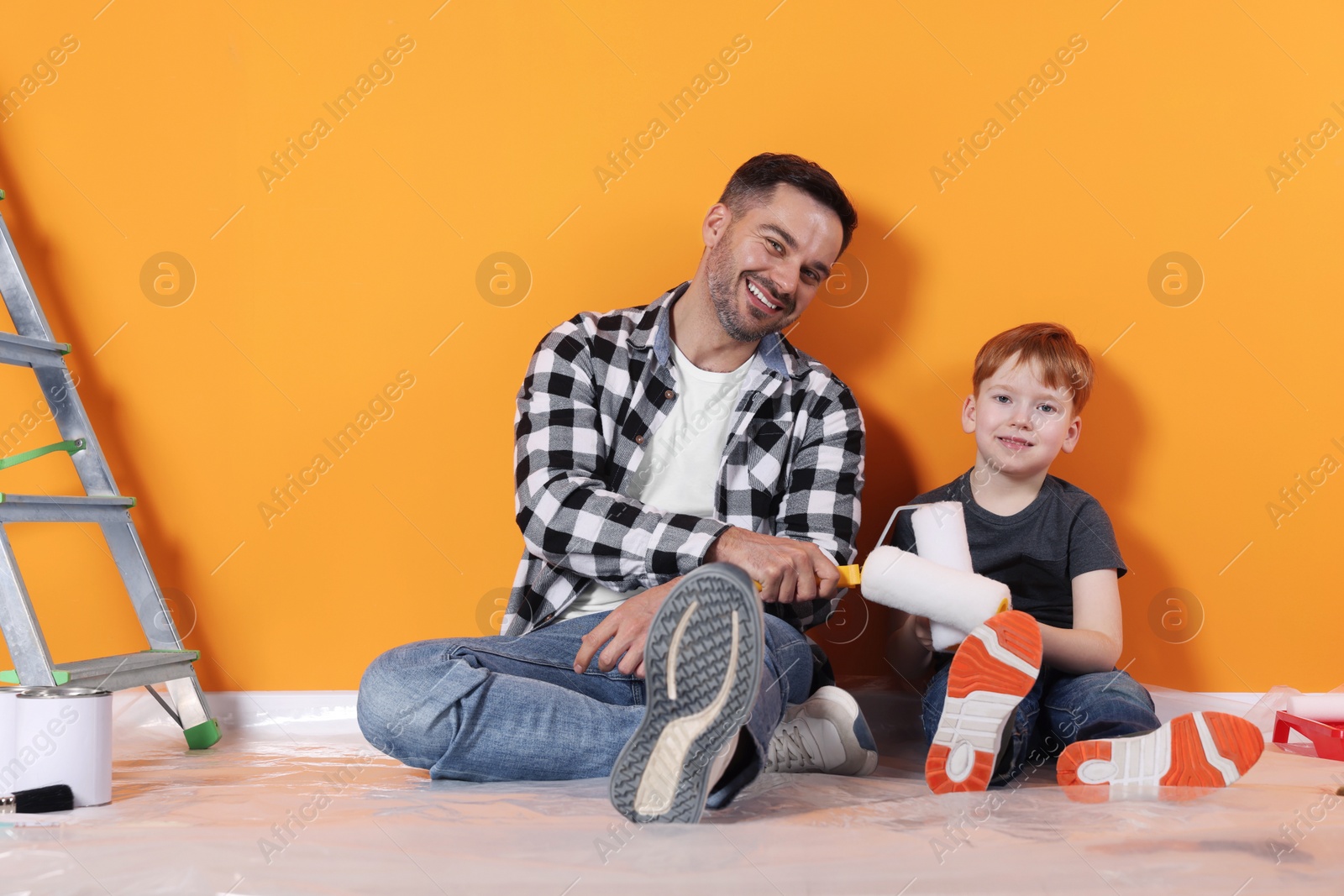 Photo of Father and son with rollers near orange wall. Repair work