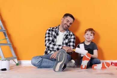 Father and son with rollers near orange wall. Repair work