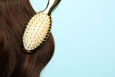 Photo of Stylish brush with brown hair strand on light blue background, top view. Space for text