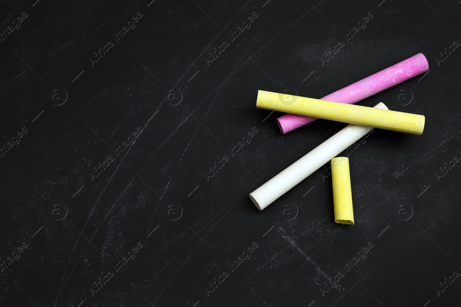 Photo of Colorful chalks on black board, flat lay. Space for text